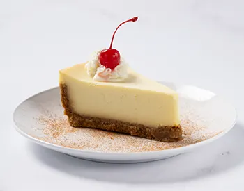 New York style cheesecake with a graham cracker crust, topped with glazed cherries for a sweet and tangy dessert finish.