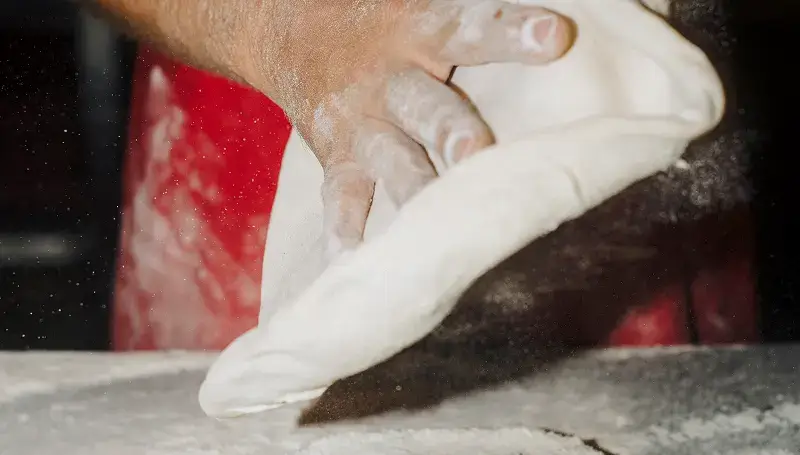 A chef stretching pizza dough, highlighting the skilled team at Anthony’s Coal Fired Pizza, dedicated to delivering quality meals.