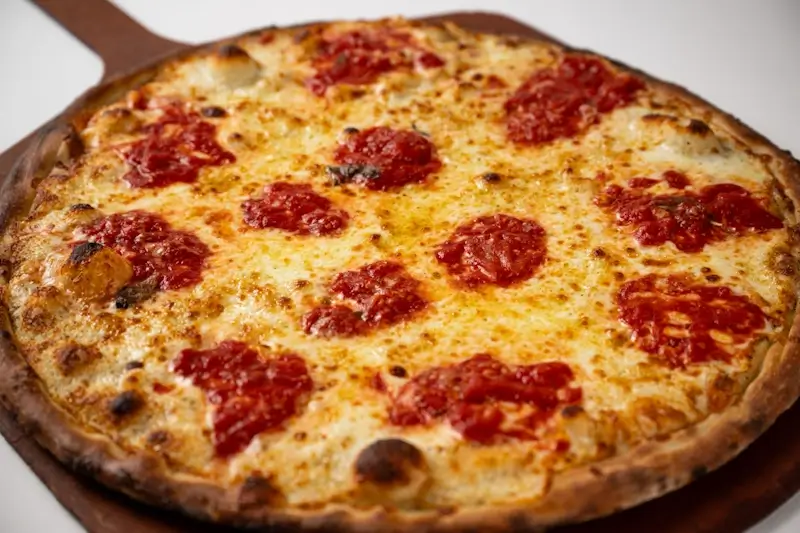 Coal fired cheese pizza with dollops of tangy tomato sauce and a golden, blistered crust, showcasing Anthony’s signature crisp and smoky finish.