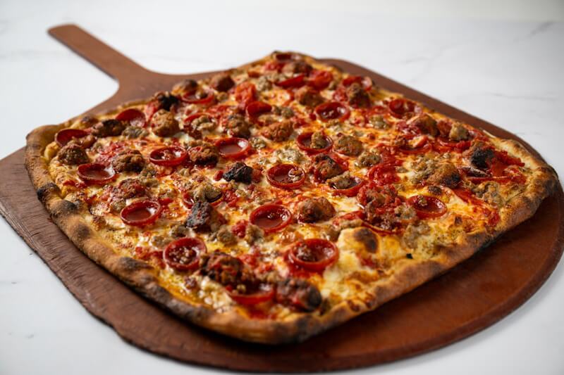 Square coal fired pizza piled with pepperoni, crumbled sausage, and meatballs, delivering a smoky, meat-lover’s feast from Anthony’s Coal Fired Pizza.