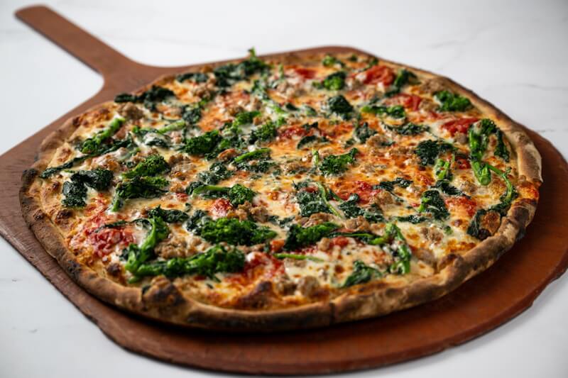 Coal fired pizza layered with crumbled Italian sausage, charred broccoli rabe, and golden cheese, delivering bold, smoky flavor in every bite.