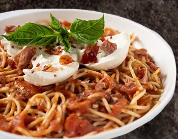 Spaghetti topped with creamy burrata, prosciutto, and tomato sauce at Anthony’s, an elevated Italian pasta experience.