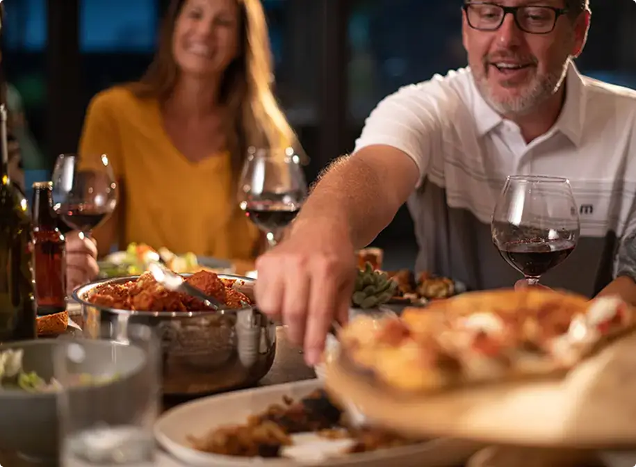 Friends sharing coal fired pizza, pasta, and wine in a cozy group setting, capturing the warmth and connection of shared dining.