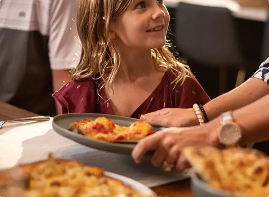 Child receiving a plate of pasta at Anthony’s Coal Fired Pizza during a cozy family meal with coal fired pizza, pasta, and starters.