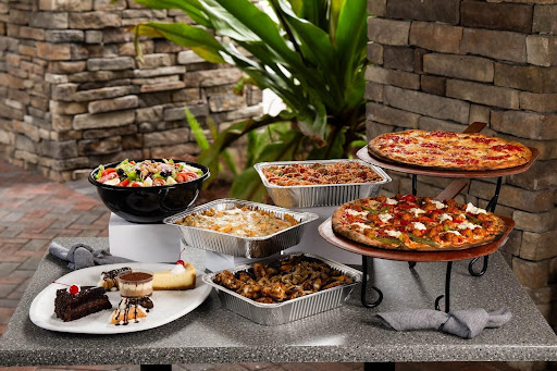 A graduation party spread with coal-fired pizza, wings, pasta, salad, and desserts from Anthony’s, perfect for a celebration.
