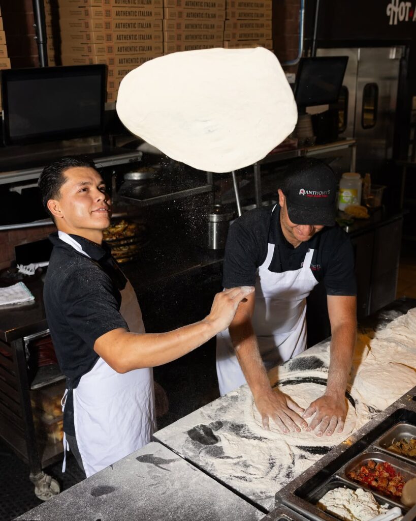 Two chefs at Anthony’s Coal Fired Pizza kneading pizza dough by hand, preparing authentic coal-fired crust.